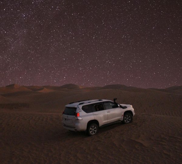 Car Parked on Sand Dunes Under the Starry Sky